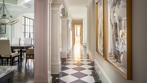 A hallway with a checkered floor, white columns, and framed artwork on the walls.