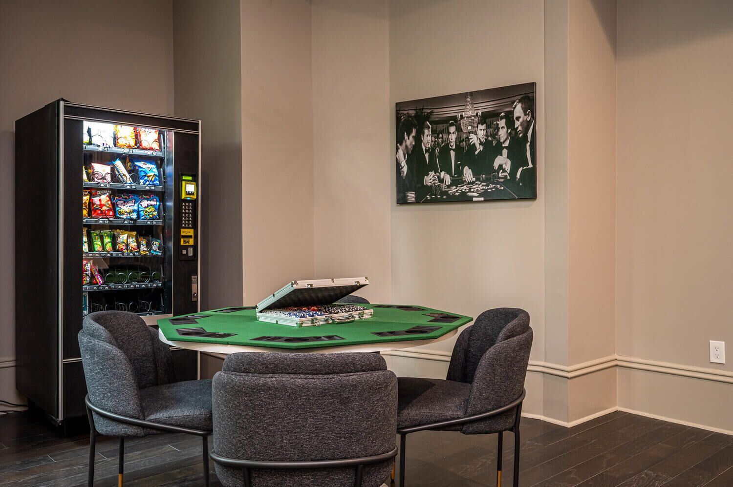 Een kamer met een pokertafel, twee stoelen, een automaat en een lijst aan de muur.