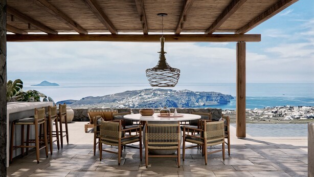 An outdoor dining area with a view of the sea and a mountainous landscape.