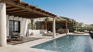 A poolside area with lounge chairs, a pergola, and a stone wall.