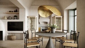 A modern dining area with a round table, four chairs, a potted plant, and a large pendant light. - Patina & Vivera Estate Santorini (Pyrgos)