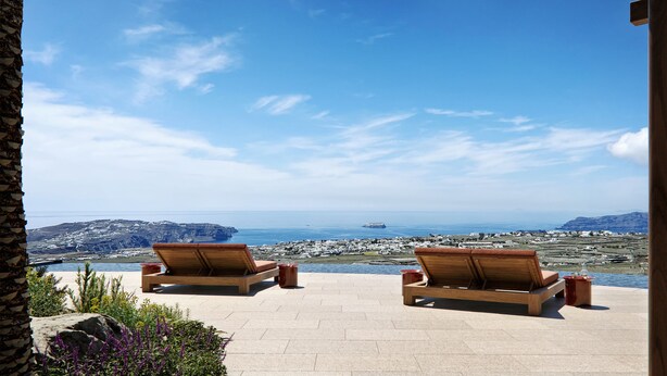 Two wooden lounge chairs facing a scenic ocean view with rocky terrain and a clear sky. - Patina & Vivera Estate Santorini (Pyrgos)