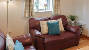 A living room with a brown leather sofa, a glass coffee table, a floor lamp, and a window with curtains.