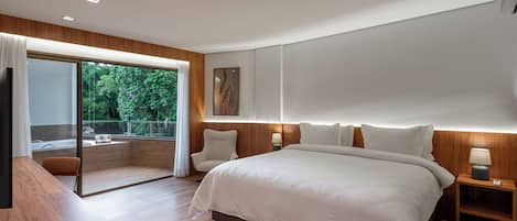 Un dormitorio moderno con una cama grande, suelo de madera, una puerta de vidrio que da a un balcón y vistas a zonas verdes.