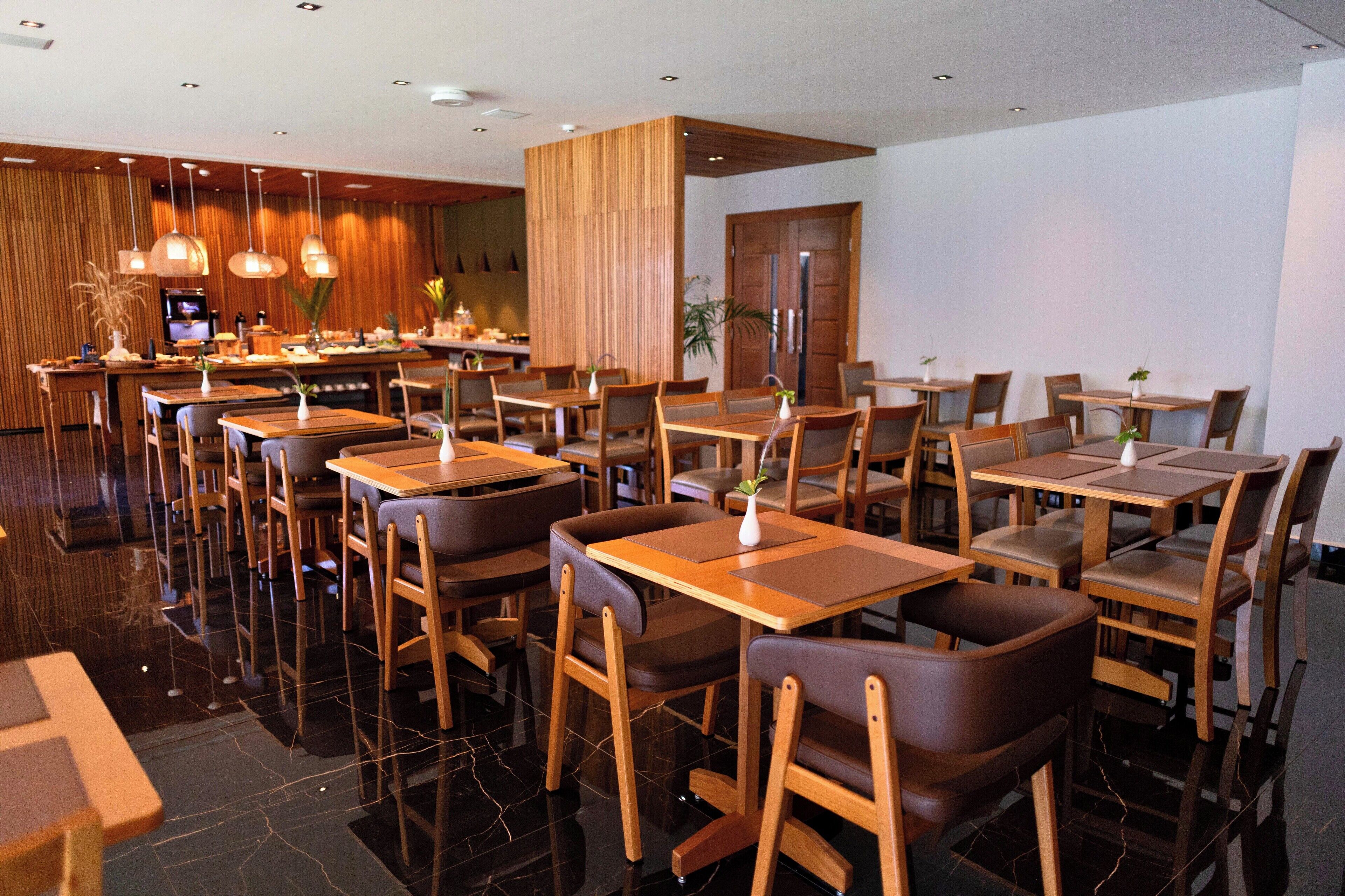 Un restaurante moderno con mesas y sillas de madera, una zona de bar y un suelo pulido.
