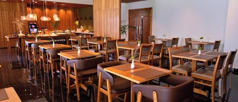 Un restaurante moderno con mesas y sillas de madera, una zona de bar y un suelo pulido.