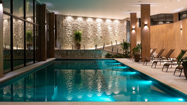 A swimming pool with a stone wall backdrop, lounge chairs, and potted plants. - Vert Hotel Spa (Itatiaia)