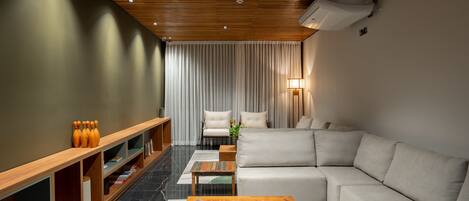 A modern living room with a wooden ceiling, a beige sofa, a wooden coffee table, and a TV stand.