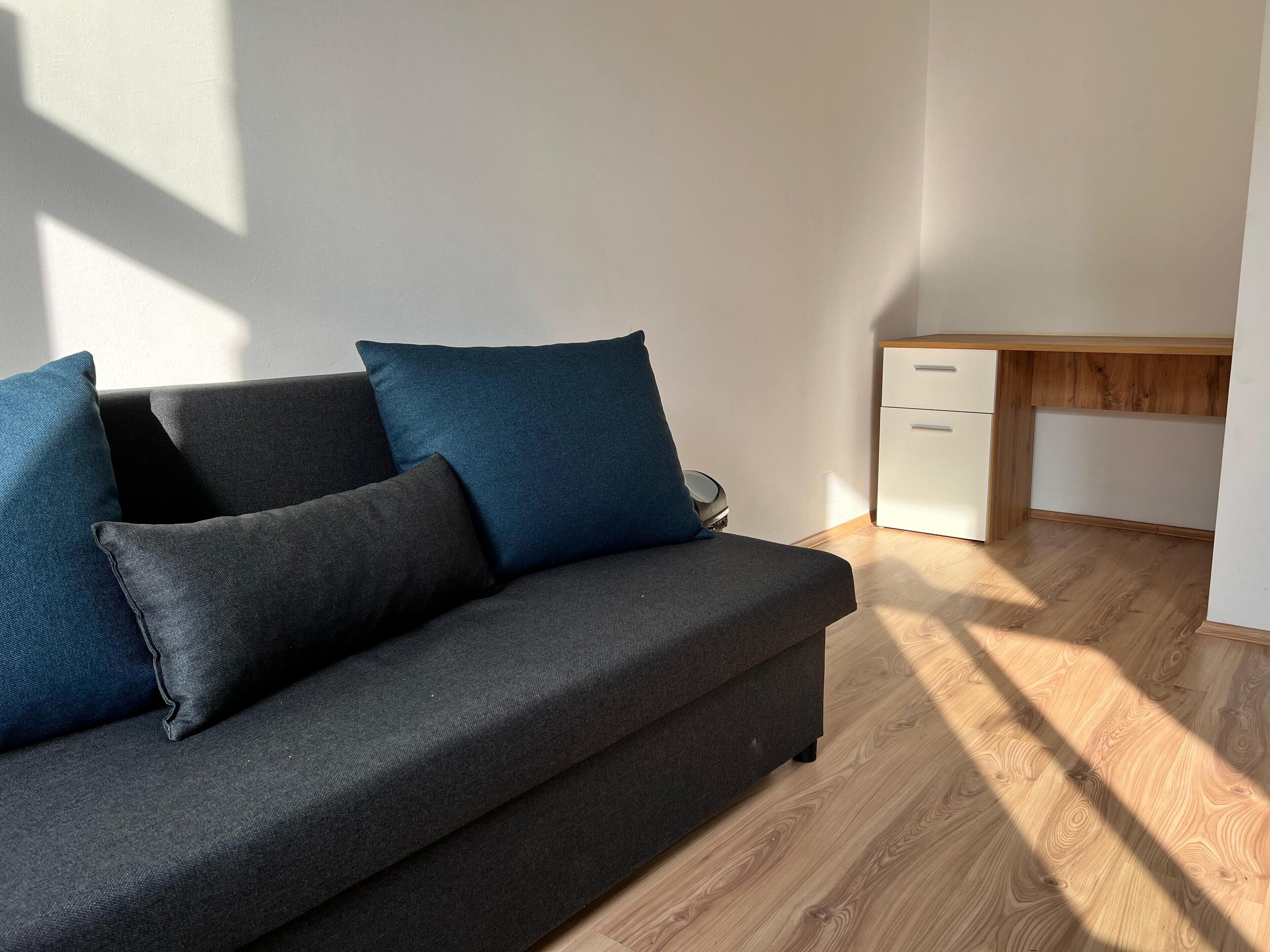 A modern living room with a dark grey sofa, blue cushions, and a wooden floor.
