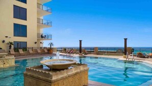 A pool area with a fountain, lounge chairs, and a view of the ocean. - Luxury Gulf View Suite with Penthouse Views! (Panama City Beach)