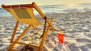 A beach chair, a pair of sandals, and a drink on the sand. - Luxury Gulf View Suite with Penthouse Views! (Panama City Beach)