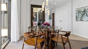 A modern dining area with a glass table, wooden chairs, and pendant lighting. - Luxury Gulf View Suite with Penthouse Views! (Panama City Beach)