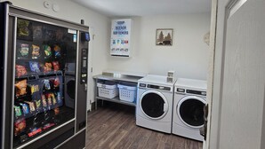 A laundry facility with a vending machine, washing machines, and a sign indicating soap, bleach, and softeners.