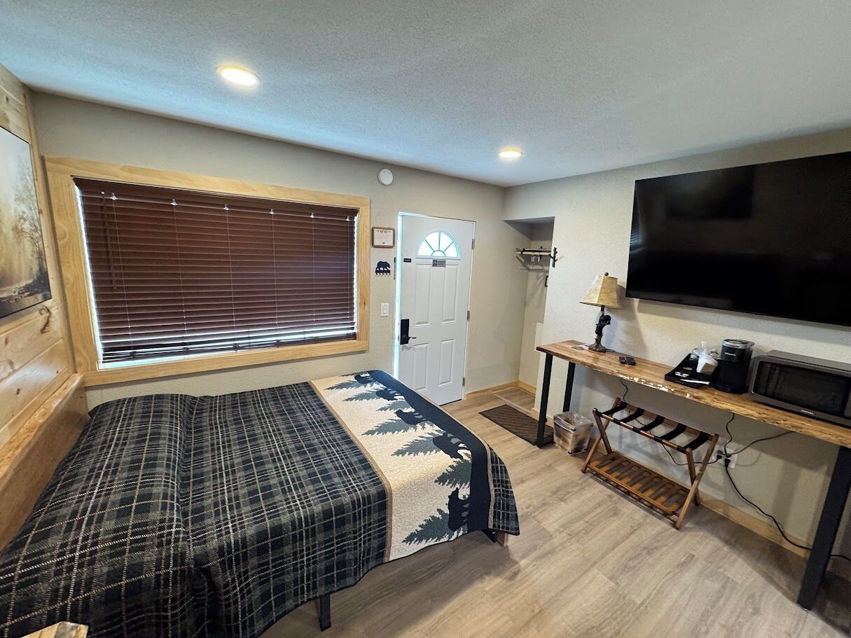 A compact room with a bed, a television, a small desk, and a door.