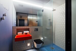 Un baño moderno con un lavabo rojo, un inodoro negro y un box de ducha de vidrio.