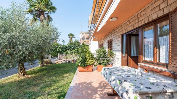 A residential building with a patio, outdoor seating, and a garden with olive trees.