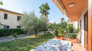 A courtyard with a table set for dining, surrounded by greenery and a building with a tiled roof.