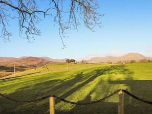 A grassy field with a fence, a clear sky, and distant mountains. - The Peacock Roost - UK46297 (Ymwlch, near Porthmadog)