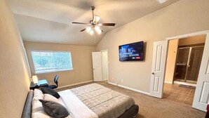 A bedroom with a bed, a ceiling fan, a TV, and a door leading to a bathroom.