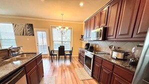 A kitchen with wooden cabinets, a granite countertop, a dining table with chairs, and a chandelier.