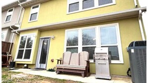 A two-story yellow building with multiple windows, a front door, and a patio area with outdoor furniture.