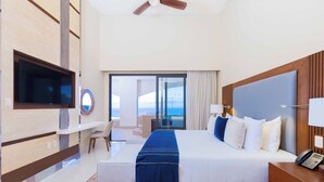 A modern hotel room with a large bed, a flat-screen TV mounted on the wall, a desk with a chair, and a view of the ocean through the balcony doors. - Amazing 3-bedroom condo with pool, fitness room, in phenomenal Chileno Bay, Cabo (San José del Cabo)
