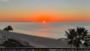A beach view with a sunset, palm trees, and a boardwalk with seating areas. - Amazing 3-bedroom condo with pool, fitness room, in phenomenal Chileno Bay, Cabo (San José del Cabo)