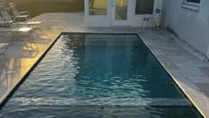Piscina retangular com água cristalina, rodeada por um deck de pedra.
