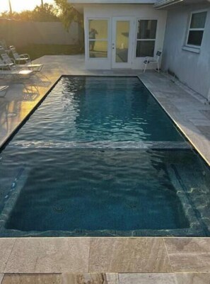 Ein rechteckiger Swimmingpool mit klarem Wasser, umgeben von einer Steindeckfläche.