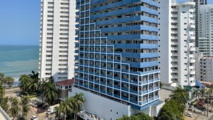 A modern multi-story hotel with a blue and white facade, located near a beach with palm trees and a clear view of the ocean. - Apartamentos en Edificio Portofino ICDI (Cartagena)