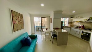 A modern apartment with a teal sofa, a dining area, a kitchen with a central island, and a balcony with a city view. - Apartamentos en Edificio Portofino ICDI (Cartagena)