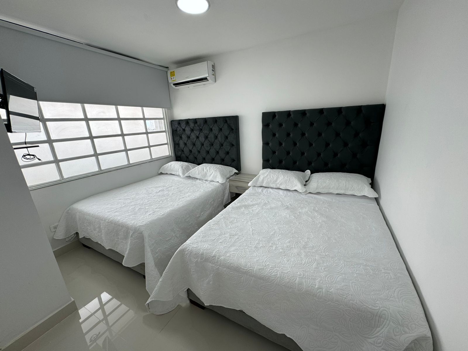 Une chambre d’hôtel avec deux lits simples, une grande fenêtre et un appareil de climatisation.