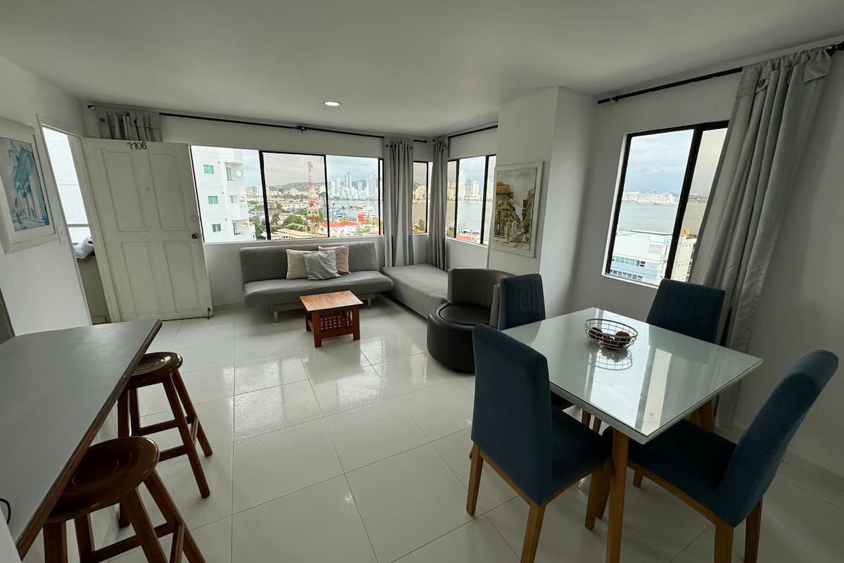 A modern living room with a dining area, large windows with city views, and a sofa.