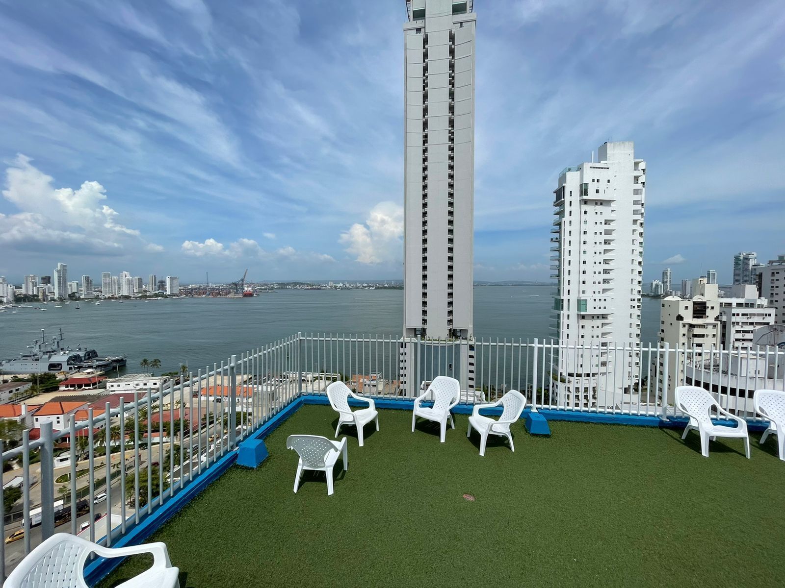 Una terrazza sul tetto con sedie di plastica bianca e vista sullo skyline cittadino e sul mare.