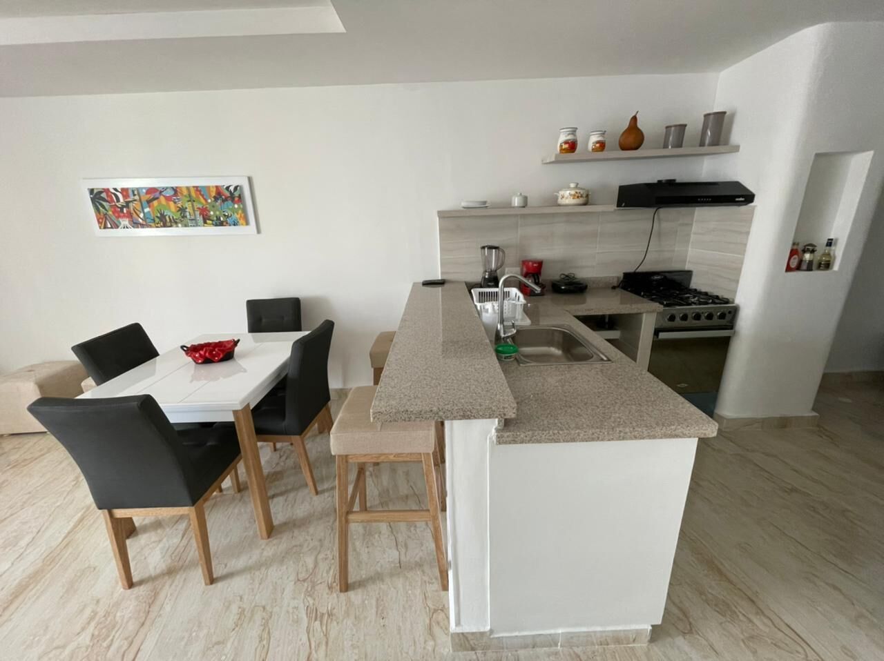 A modern kitchen with a central island, dining table, chairs, and a stove.
