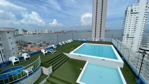 A rooftop pool with two separate sections, surrounded by white lounge chairs and a view of the city and sea. - Apartamentos en Edificio Portofino ICDI (Cartagena)