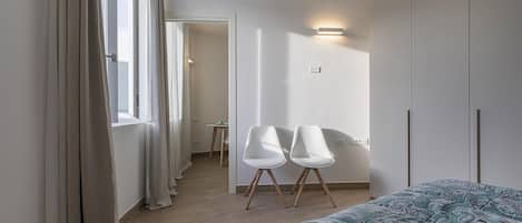 Une chambre à coucher avec un lit, deux chaises blanches, une petite table et une armoire.
