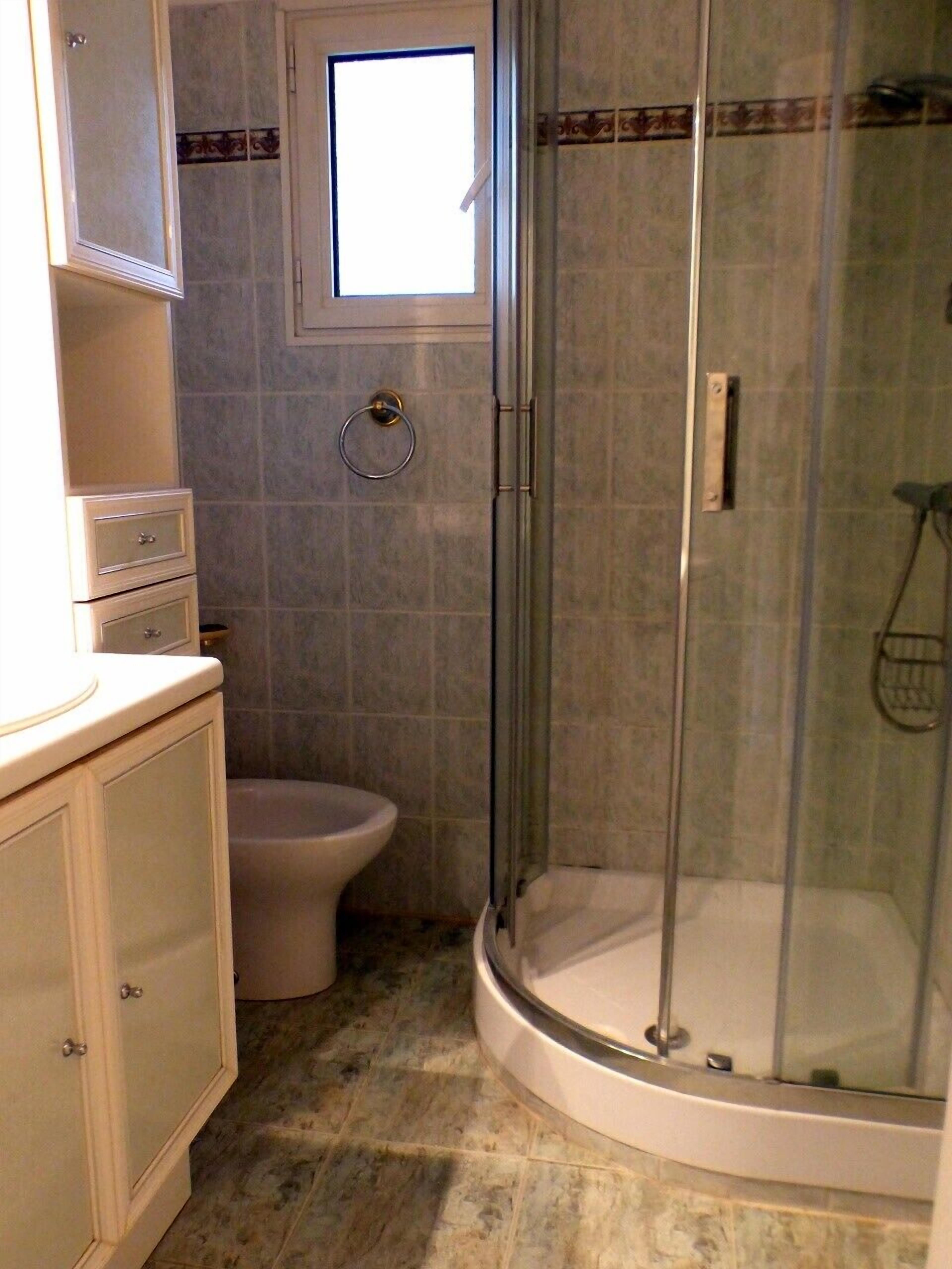 A bathroom with a glass-enclosed shower, a toilet, and a small window.
