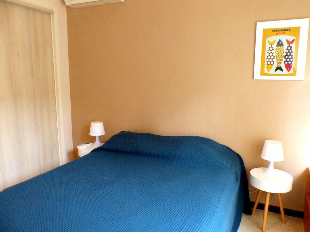 A hotel room with a large bed, two bedside tables with lamps, a framed picture on the wall, and a window with blinds.
