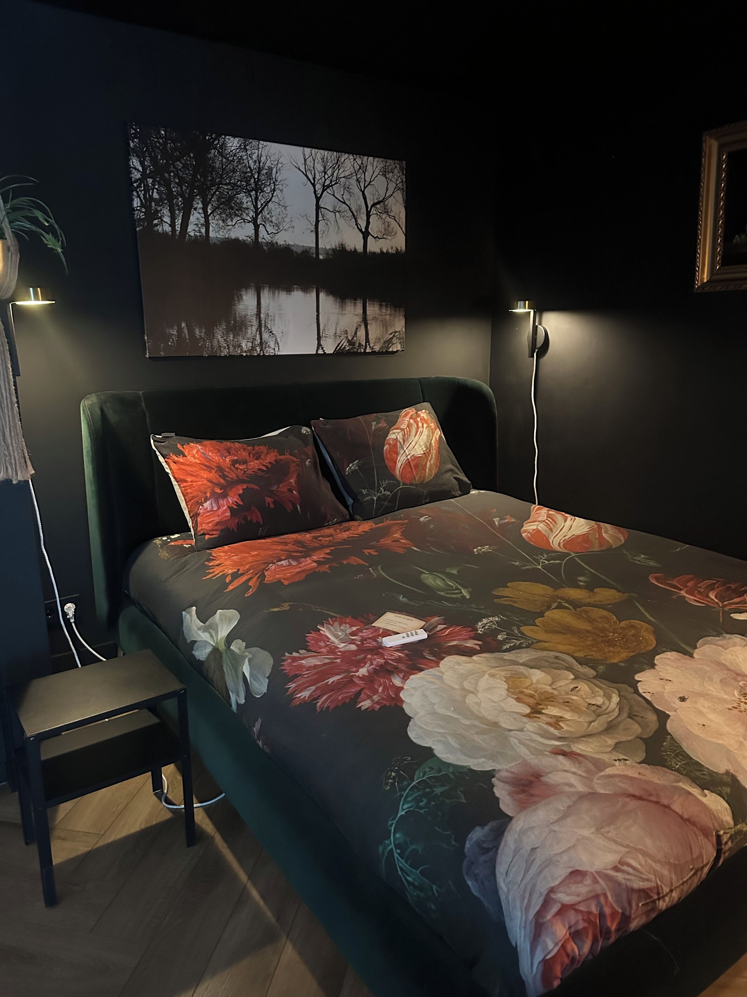A bedroom with a bed, two bedside lamps, a small table, and a wall-mounted painting.
