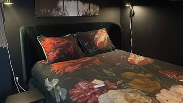 A bedroom with a bed, two bedside lamps, a small table, and a wall-mounted painting.