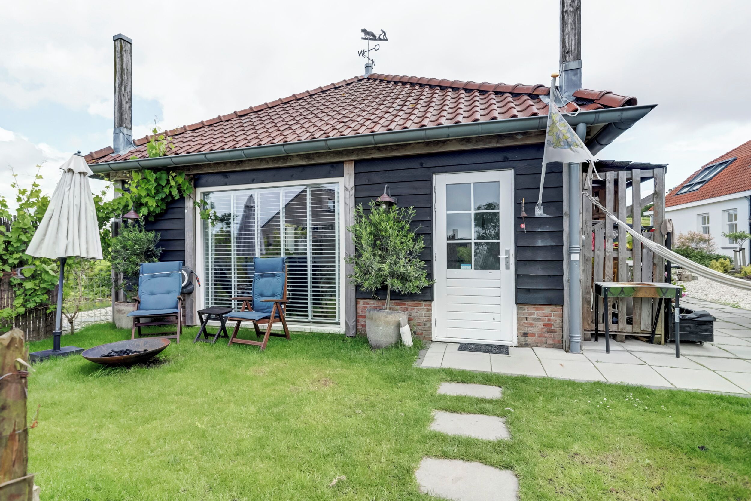A house with a red-tiled roof, a front door, and a small patio area with a chair and a table.