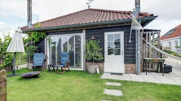 A house with a red-tiled roof, a front door, and a small patio area with a chair and a table.