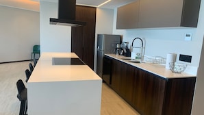 Uma cozinha moderna com uma ilha central, armários de madeira escura, forno embutido e geladeira de aço inoxidável.