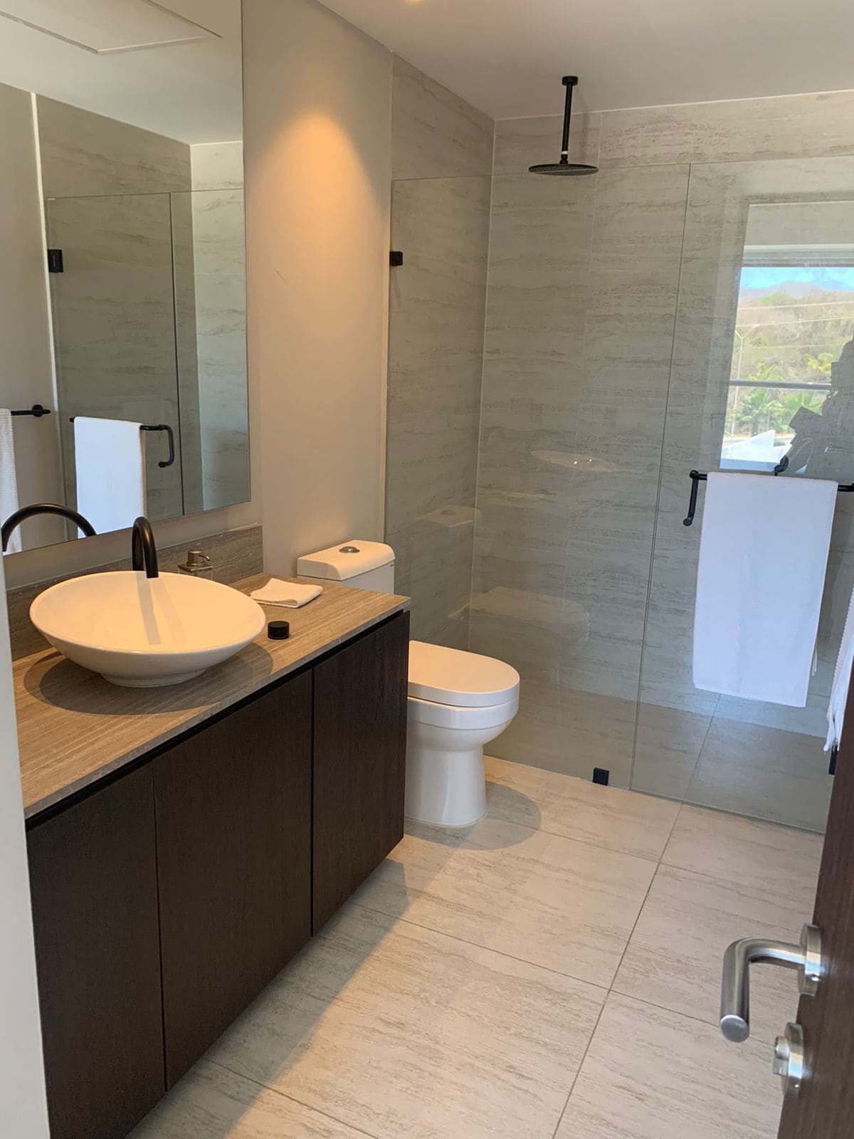 Een moderne badkamer met een grote spiegel, een rond wastafeltje, toilet en een douchehoek.