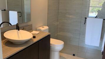 Een moderne badkamer met een grote spiegel, een rond wastafeltje, toilet en een douchehoek.