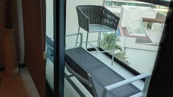 Un balcón con una silla, una mesa, una planta en maceta y vistas a un edificio moderno.