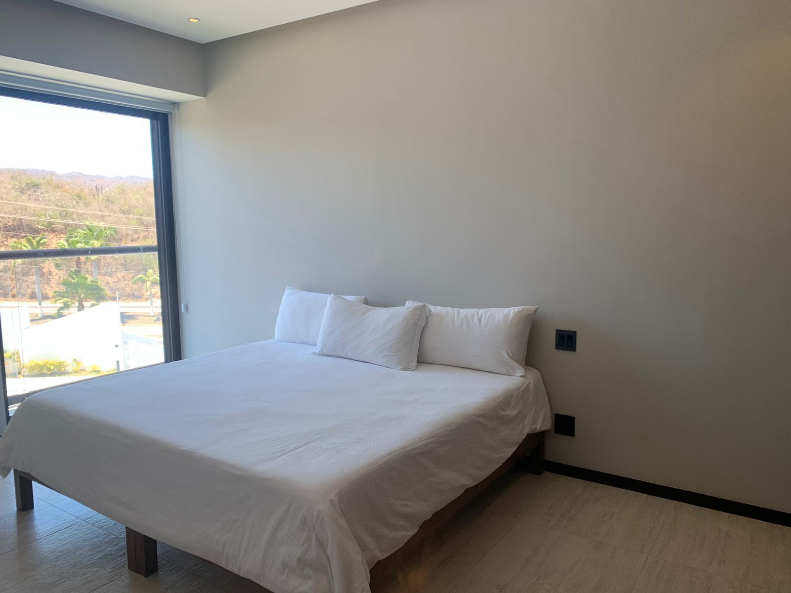 Un dormitorio moderno con una cama grande, una ventana que ofrece vistas a un paisaje, y un diseño minimalista.