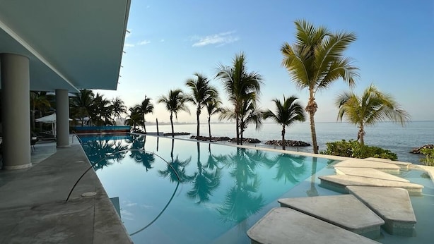 Piscina com água cristalina, palmeiras e vista para o mar.