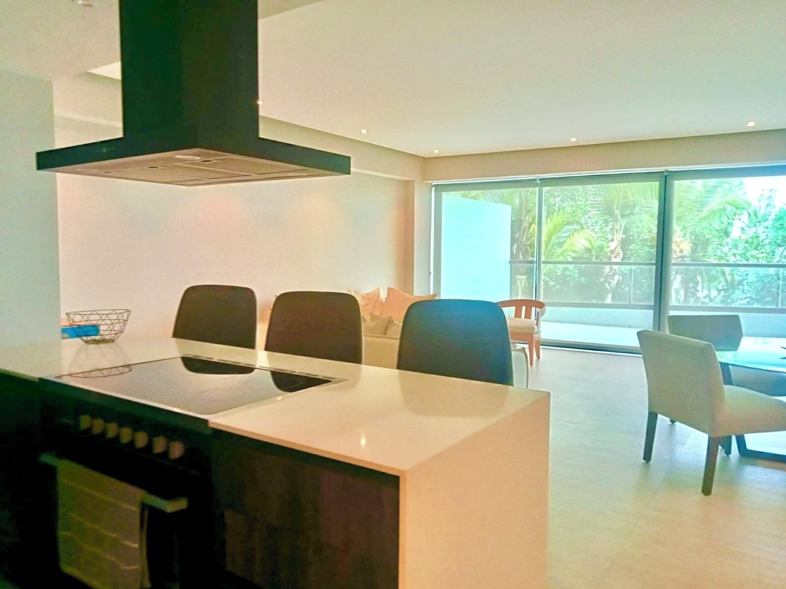 Una cocina moderna con una isla central, estufa y un amplio ventanal con vistas a zonas verdes.